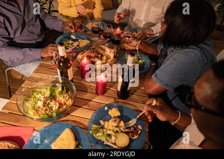 Amici anziani multiculturali che mangiano cibo e vino con candele sul tavolo da pranzo Foto Stock