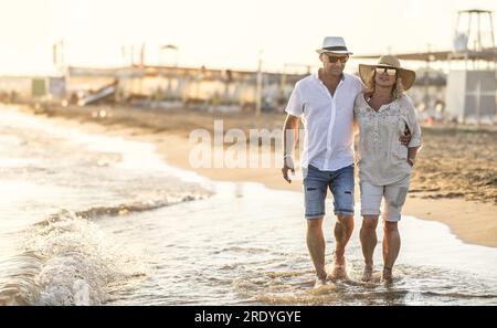 Una coppia di mezza età che cammina mano nella mano sulla spiaggia al tramonto. Foto Stock
