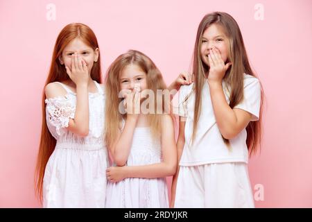 Ritratto di ragazze allegri, bambini che coprono la bocca con le mani, sorridono nascosto e ridono sullo sfondo rosa dello studio Foto Stock