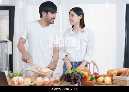 Un uomo sorridente che abbraccia una donna, due persone in piedi e si guardano con gioia. Una giovane coppia è felice di trascorrere il proprio tempo a casa in un'accogliente cucina moderna. Foto Stock