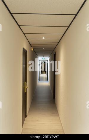 Vista di un lungo corridoio vuoto dell'hotel con plafoniere illuminate e porte chiuse Foto Stock