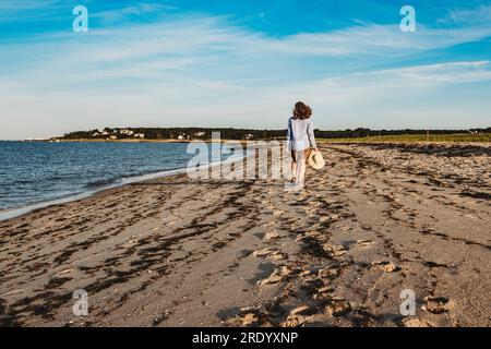 Donna matura che cammina sulla spiaggia di Cape Cod in estate con cappello in mano Foto Stock