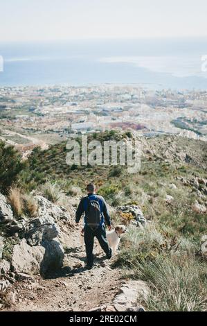 Uomo che cammina lungo una collina con un cane che si affaccia sulla città e sull'oceano di Malaga Foto Stock