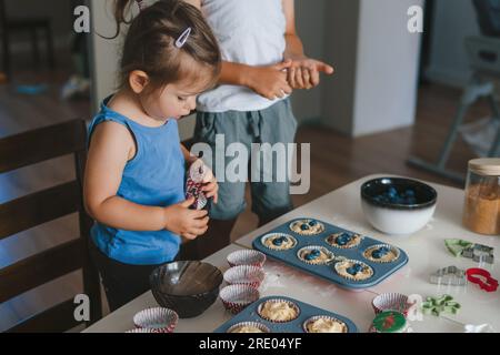 Due bambini imparano a cucinare, versando l'impasto in stampi speciali per cuocere i cupcake porzionati, mettendo i mirtilli rossi nell'impasto. Fare torte e. Foto Stock