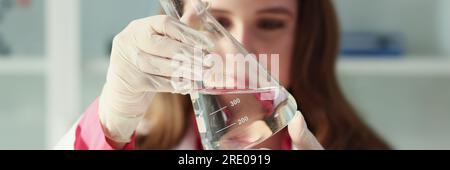 Una giovane donna assistente di laboratorio guarda l'acqua del pallone Foto Stock