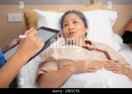 Closeup mani infermiere scrivere rapporto documento su prescrivere assistenza medica e sanitaria su tablet durante il controllo e la diagnosi con paziente anziano in hospi Foto Stock