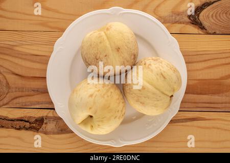 Tre pesche mature organiche con piastra in ceramica bianca su tavolo in legno, macro, vista dall'alto. Foto Stock