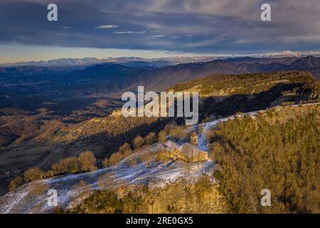 Vista aerea delle scogliere e del santuario di Cabrera all'alba invernale con neve a Collsacabra (Osona, Barcellona, Catalogna, Spagna) Foto Stock