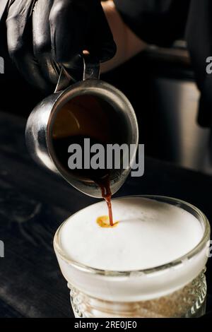 barista con guanti in lattice che prepara latte macchiato, versa l'espresso, caraffa con caffè, macro Foto Stock