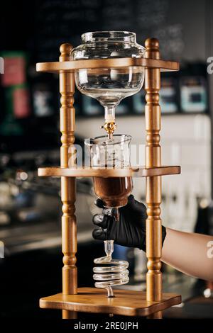 barista con guanto nero che assembla la macchina per il caffè americano freddo con caffè macinato e un'altra preparazione di caffè espresso Foto Stock