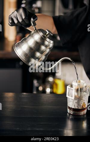 barista che prepara l'espresso, versando acqua bollente dal bollitore nel bicchiere con il caffè nel sacchetto del filtro Foto Stock