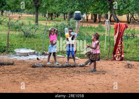 Villaggio africano, bambini felici che giocano nel cortile con bottiglie riciclate, divertimento per tutta la famiglia Foto Stock