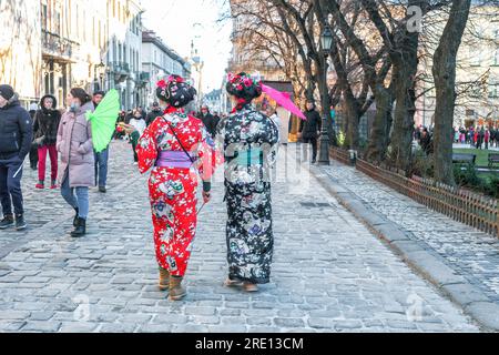 Leopoli, Ucraina - 7 gennaio 2022: Due giovani donne in kimono tradizionale giapponese con ombrelloni che camminano per la città, vista posteriore Foto Stock