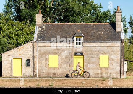 Ciclista su una bici elettrica che passa davanti alla casa numero 3 del guardiano della serratura Signan Sant Mikael, Saint Michel, sul fiume Blavet a Pontivy (Bri Foto Stock
