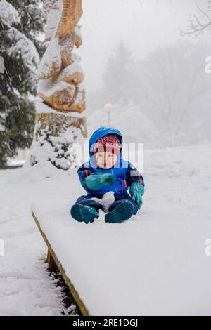 bambino di 11 mesi seduto sulla neve indossando la tuta da neve Foto Stock