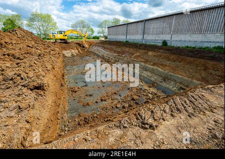 Costruzione di una fossa di letame, installazione di geomembrane, per la raccolta degli effluenti animali da un caseificio. Macchinari per cantieri edili e lavori di livellamento, mec Foto Stock