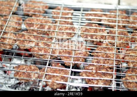 Polpette alla griglia kofta kufta di carne macinata di manzo in una rete a rete grigliata con manico su un carbone con fuoco e fuoco alla griglia, barbecue succoso Foto Stock