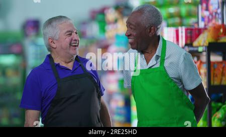 Lavoratori anziani soddisfatti e diversificati che si trovano in un negozio di alimentari sorridendo davanti alla macchina fotografica indossando uniformi. Lavoratori del personale brasiliano più anziani Foto Stock