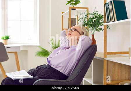 Donna d'affari adulta e sognante soddisfatta in ufficio, che si sente calma dopo aver finito il lavoro. Foto Stock