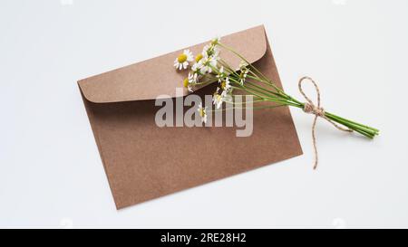 Composizione minima, mockup per biglietti d'auguri o inviti per le vacanze, appartamento, spazio per le copie. Busta marrone per artigianato, carta vuota per testo, filiale camomilla. Weddi Foto Stock