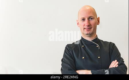 Cuoco calvo maschio isolato su sfondo bianco con spazio per la copia. Un uomo caucasico sorridente che indossa un'uniforme nera. Shot medio verticale. Foto di alta qualità Foto Stock