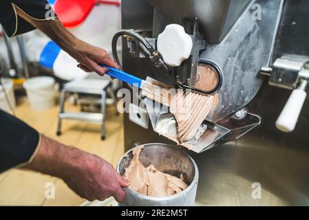 Concetto di Ice Making. Primo piano all'interno di un lavoratore professionista che utilizza una gelatiera e raccoglie il prodotto in un contenitore di acciaio. Macchina per il gelato utilizzata in cucina. Foto di alta qualità Foto Stock