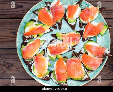 Set di bruschette con pane di segale, salmone e formaggio cremoso su uno sfondo naturale di legno scuro Foto Stock