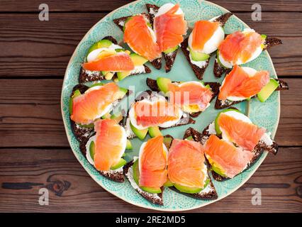 Set di bruschette con pane di segale, salmone e formaggio cremoso su uno sfondo naturale di legno scuro Foto Stock