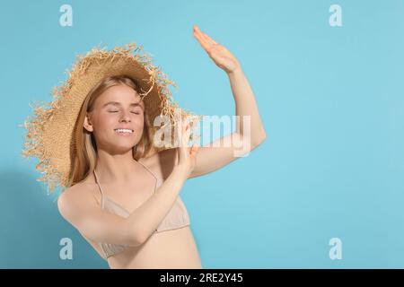 Bella giovane donna con cappello di paglia che si ombreggiava con le mani dalla luce del sole su sfondo azzurro, spazio per il testo Foto Stock