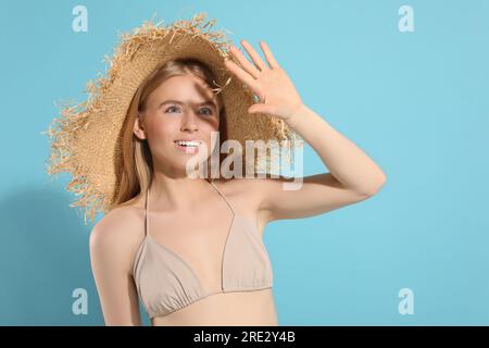 Bella giovane donna con cappello di paglia che si ombreggiava con la mano dalla luce del sole su sfondo azzurro. Spazio per il testo Foto Stock