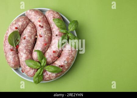 Salsicce crude fatte in casa, foglie di basilico e grani di pepe sul tavolo verde, vista dall'alto. Spazio per il testo Foto Stock