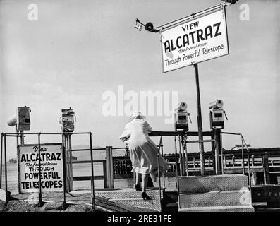 San Francisco, California: c. 1953. Una donna curiosa dà un'occhiata attraverso un telescopio attraverso la baia di San Francisco nella prigione federale sull'isola di Alcatraz. Foto Stock