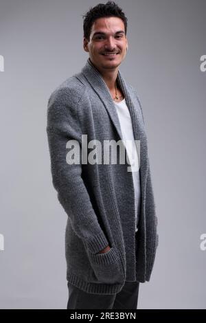 Bel giovane, alto, con capelli neri corti, baffi leggeri e barba leggera. Sta ridendo, indossando una giacca di lana sopra una t-shirt bianca. Muscolare Foto Stock