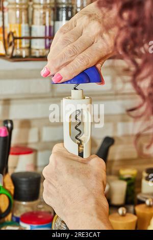 Donna apre una bottiglia di vino bianco con un cavatappi speciale. Foto Stock