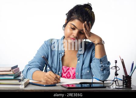 Un giovane studente indiano che studia e scrive su un tavolo da studio e su uno sfondo bianco Foto Stock