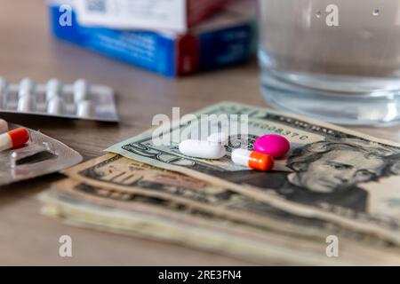 Un concetto di costo medico con un bicchiere d'acqua, varie medicine e banconote in dollari americani. Foto Stock