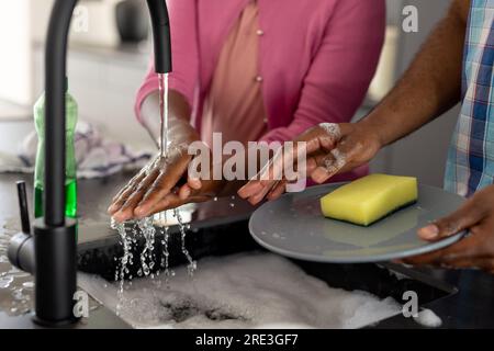 Mani di padre e figlia afroamericani che lavano i piatti in cucina a casa Foto Stock