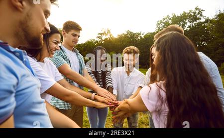 Gruppo di allegri giovani amici che si accatastano le mani mentre si divertono nel parco. Foto Stock