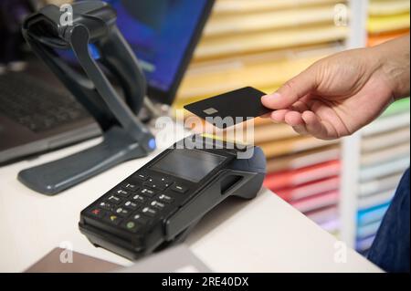 Donna in possesso di una carta di credito mockup nera vuota con spazio pubblicitario, sopra un terminale POS, lettore di carte di credito, pagamento online con NFC senza contanti. Foto Stock