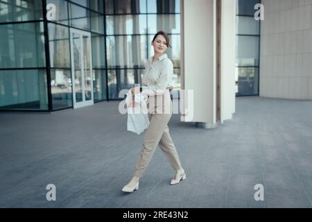 Bella donna bionda caucasica che va a lavorare nell'edificio degli uffici, tranquillo stile d'affari beige Foto Stock