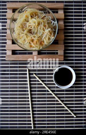 Spaghetti di riso coreani con carne e spezie in una ciotola di vetro. Deliziosi spaghetti con carne e spezie. Bastoncini di noodle coreani e salsa. Foto Stock