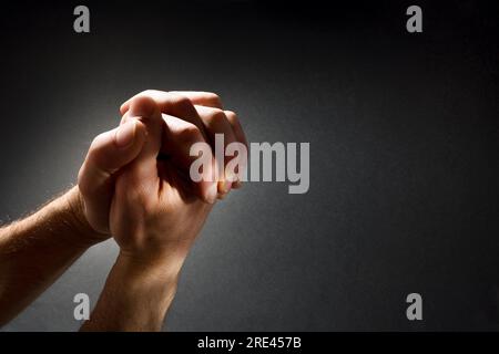 Pregare le mani dell'uomo con le dita interbloccate in contrasto con il fascio di luce su sfondo gradiente isolato scuro. Vista dall'alto in alto. Foto Stock