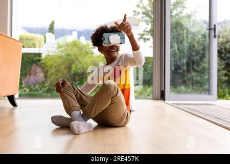 Felice ragazzo afro-americano seduto sul pavimento con visore vr e schermo virtuale a sfioramento Foto Stock