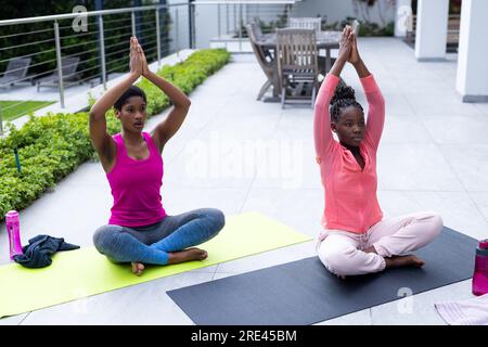 Madre e figlia afroamericane che praticano yoga sulla terrazza soleggiata a casa Foto Stock