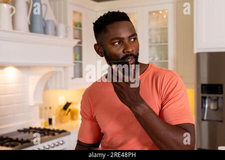 Uomo afro-americano che parla su smartphone in cucina bianca Foto Stock