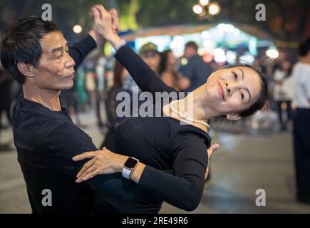 Una coppia vietnamita di mezza età vestita di danza nera per le strade di notte accanto al lago Hoan Kiem nel centro di Hanoi, in Vietnam. Foto Stock