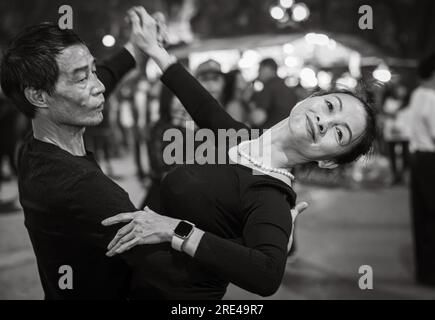 Una coppia vietnamita di mezza età vestita di danza nera per le strade di notte accanto al lago Hoan Kiem nel centro di Hanoi, in Vietnam. Foto Stock