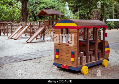 Attenzione selettiva su un'auto colorata in legno per bambini o un autobus sul terreno sabbioso di un parco giochi per bambini in un parco pubblico con un gruppo di scivoli e una p Foto Stock