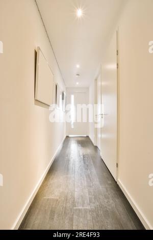 una camera bianca vuota con pavimento in legno e lampade alle pareti del corridoio è illuminata da luci a incasso Foto Stock