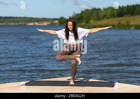 Donna che pratica yoga, esegue l'esercizio Eka Pada Agnistambha Utkatasana, Balance asana, si allena in abbigliamento sportivo mentre si trova su una gamba su un legno Foto Stock